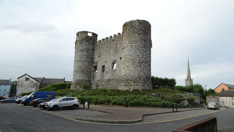 The ruined twin-towered Carlow Castle beside a car park, with the cathedral spire behind