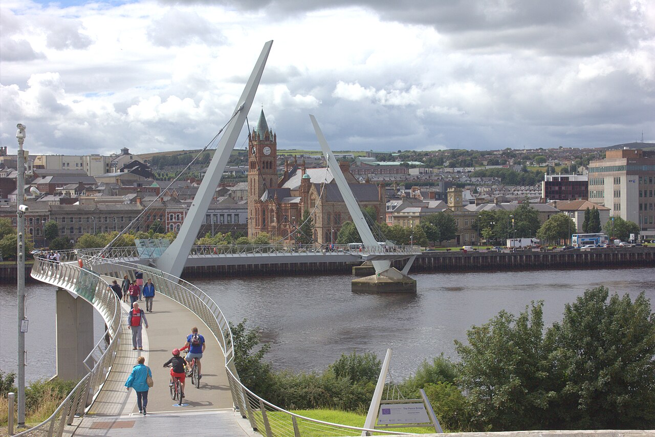 People walking and cycling across the Peace Bridge over the River Foyle, with the Guildhall clock tower on the far bank