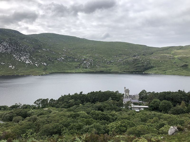 Glenveagh Castle among trees on the shore of Lough Veagh, with bare green hills behind under grey cloud