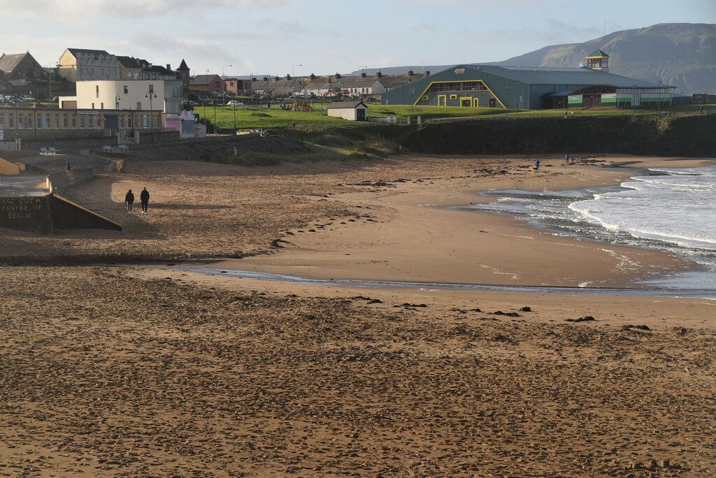 Two people walking on the wide sandy beach at Bundoran with waves on the right and the town above