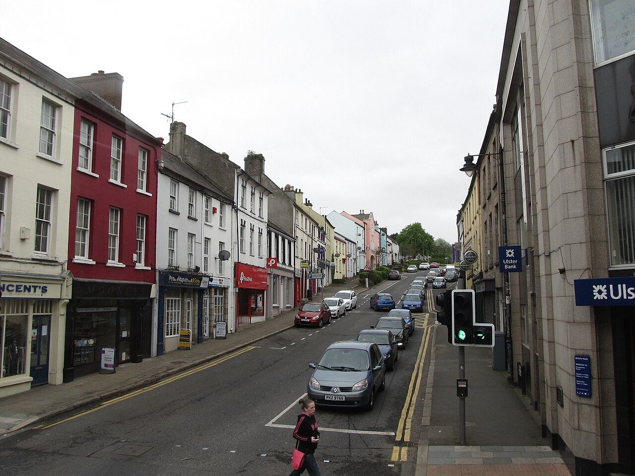 Irish Street in Downpatrick running downhill between shops and parked cars on an overcast day