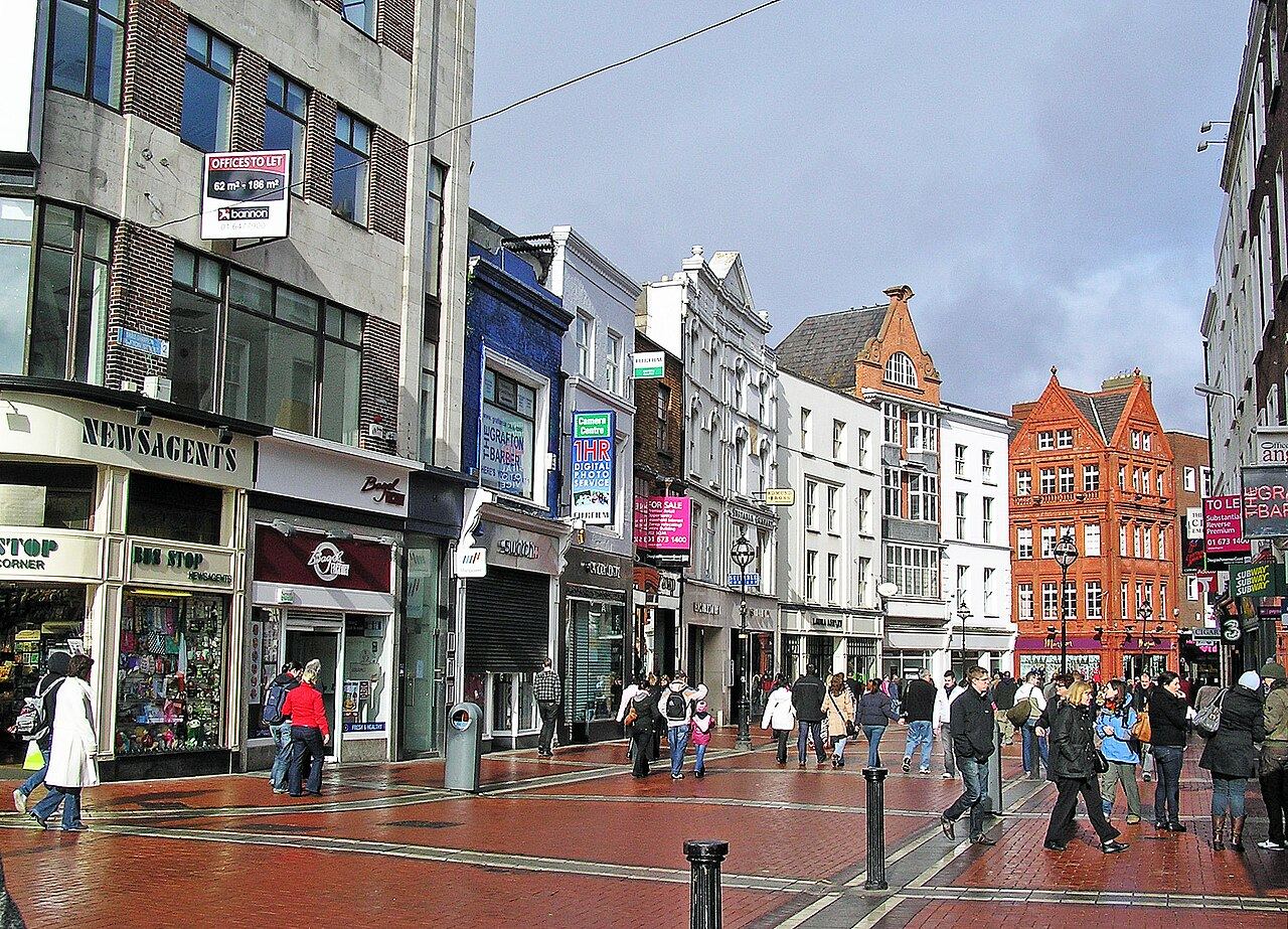 Shoppers walking along pedestrianised Grafton Street between shopfronts and red-brick buildings.