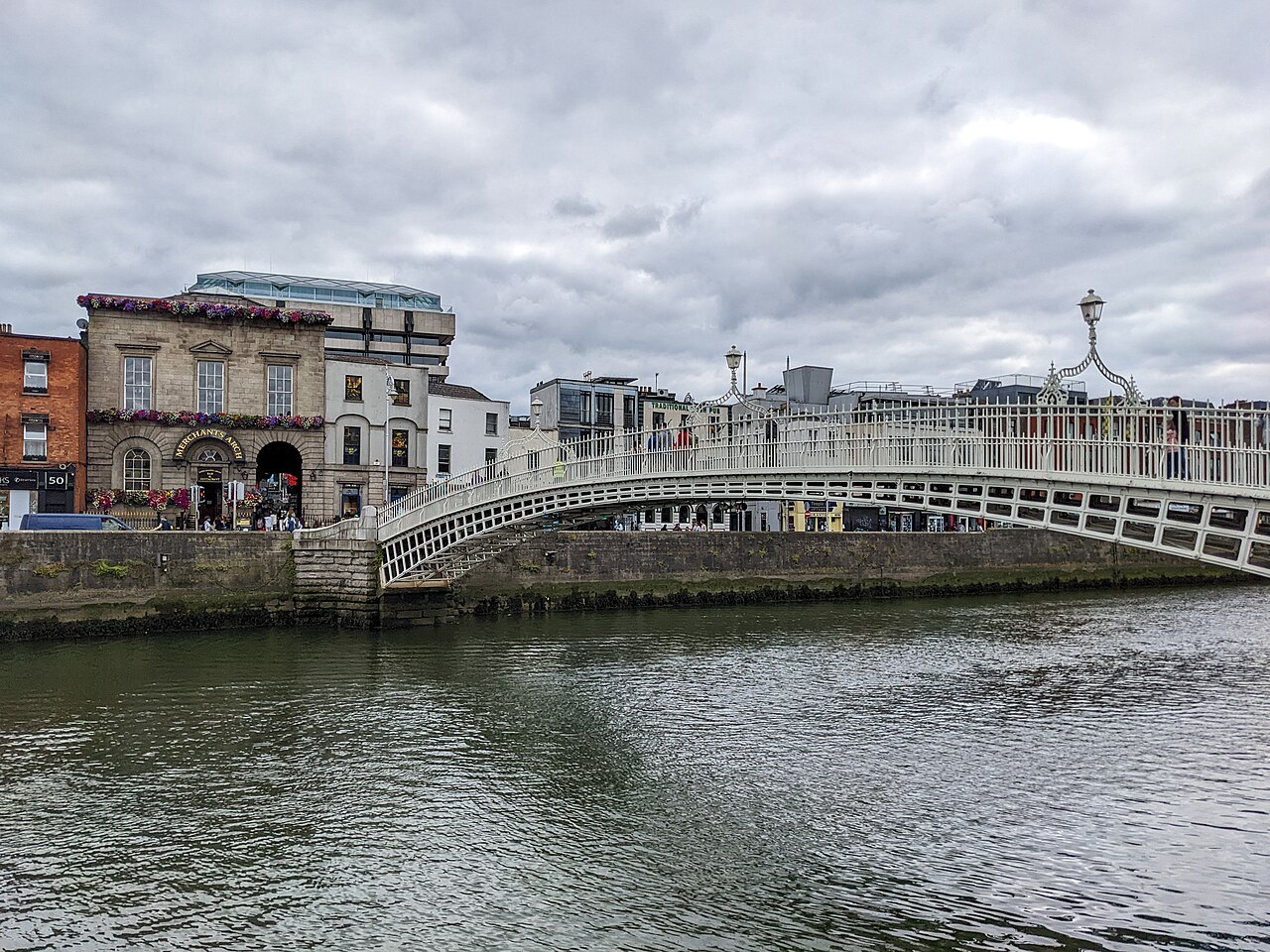 The Ha'penny Bridge over the River Liffey under a grey sky, with buildings along the quay behind.