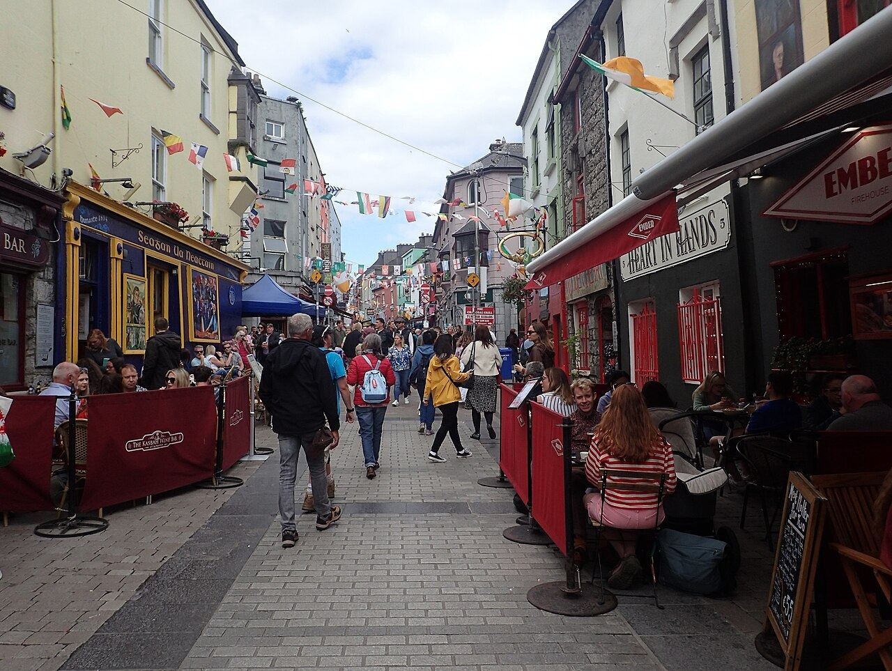 Busy pedestrian Quay Street with pub fronts, café tables and bunting