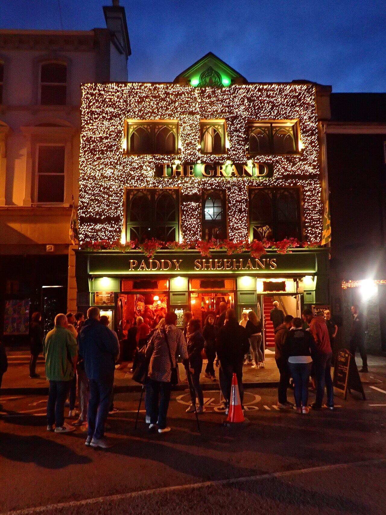 People outside a pub lit up with fairy lights in Killarney at night