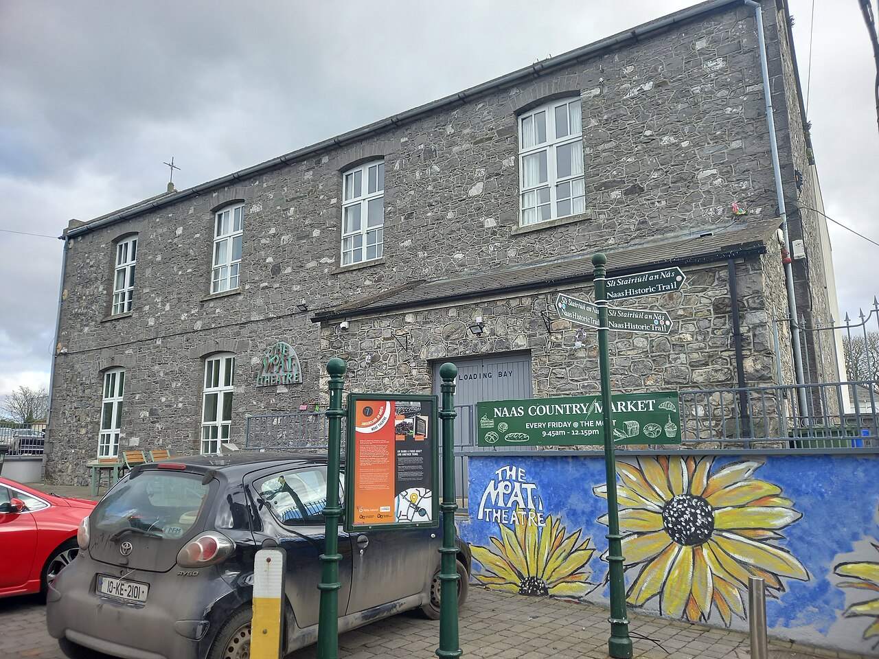The stone front of the Moat Theatre in Naas with a sunflower mural on the wall and a car parked outside