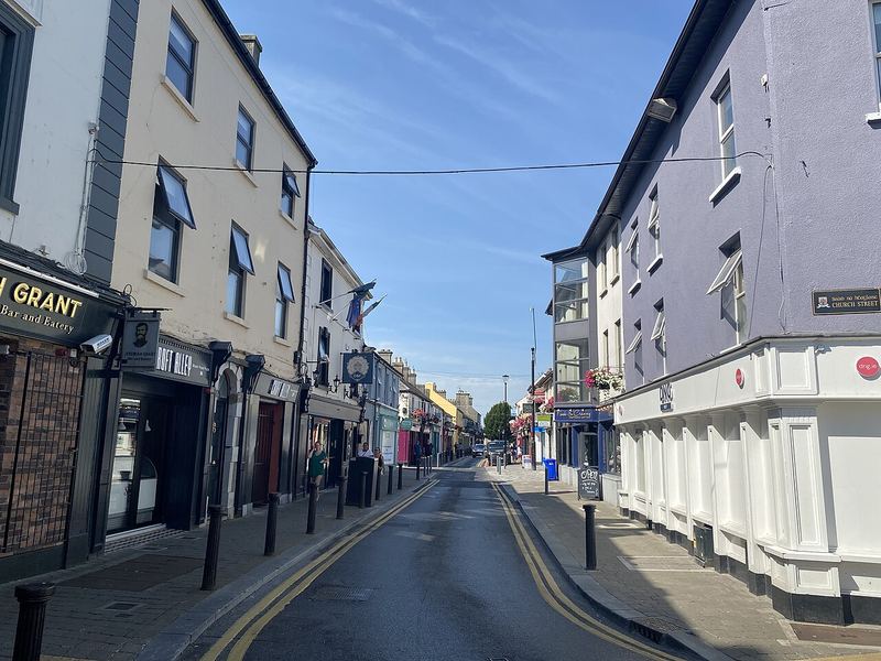 Main Street in Portlaoise on a sunny day, shopfronts and parked cars along a narrow street