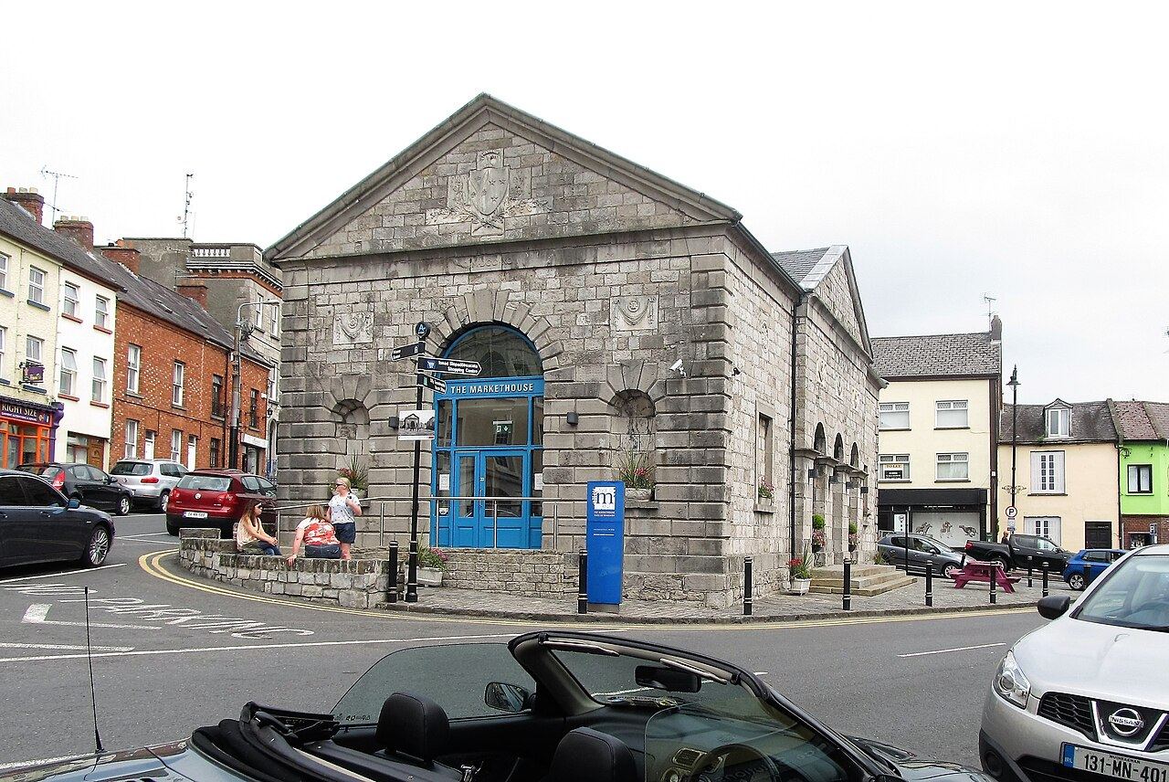 The grey limestone Market House in Monaghan town, with parked cars and people sitting on the low wall outside