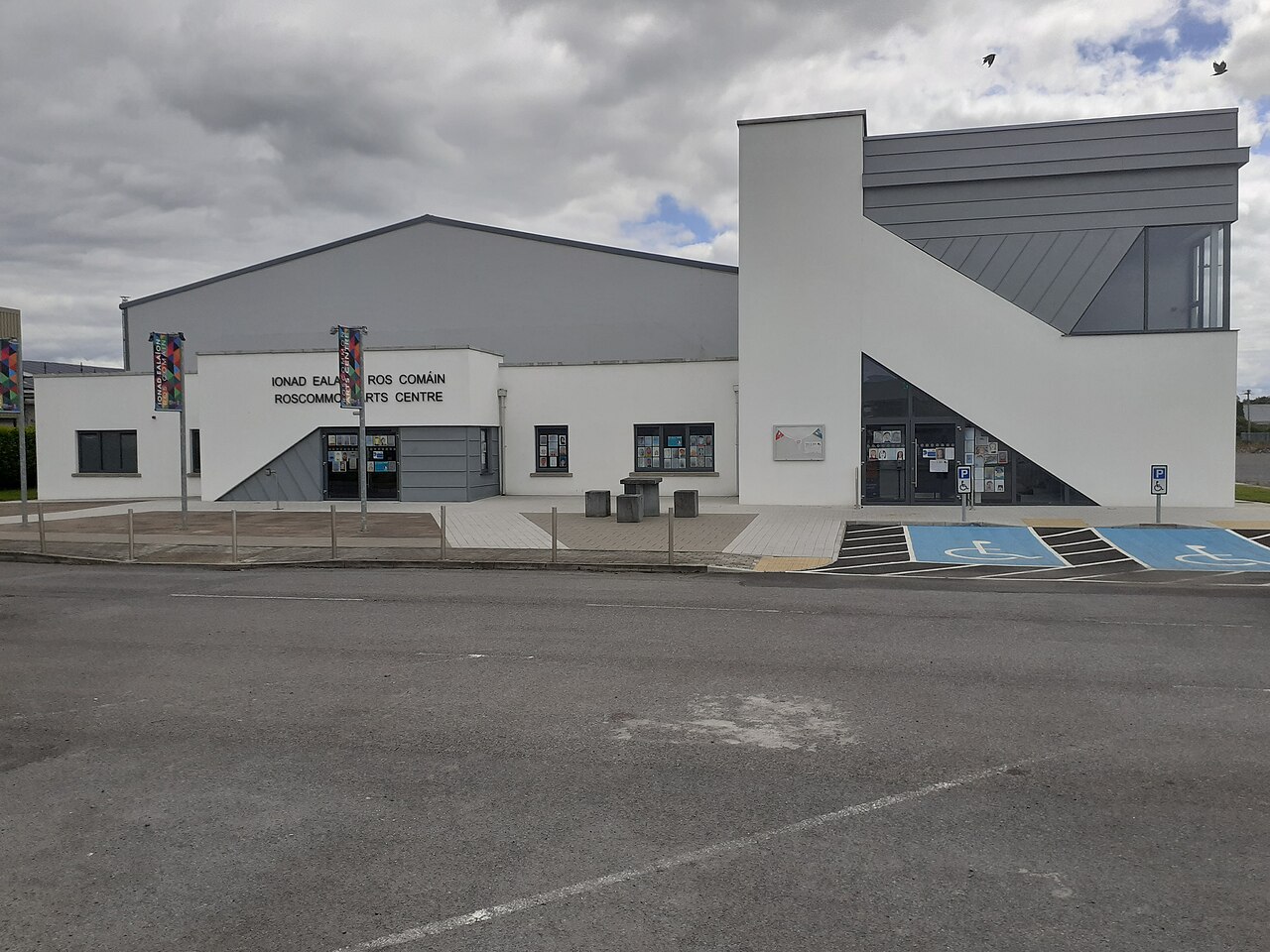 Front of Roscommon Arts Centre, a white and grey building with a bilingual sign, seen across its car park