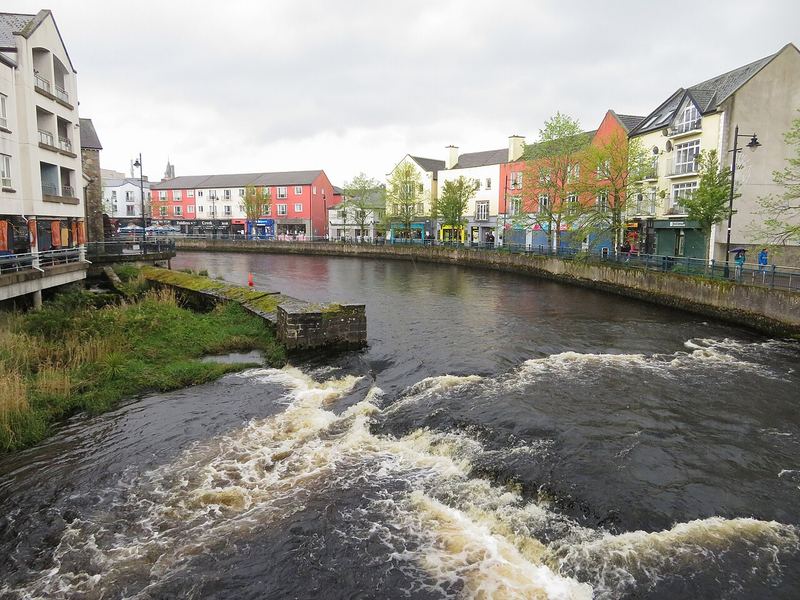 The River Garavogue running fast over a weir in Sligo town, with coloured buildings along the quay