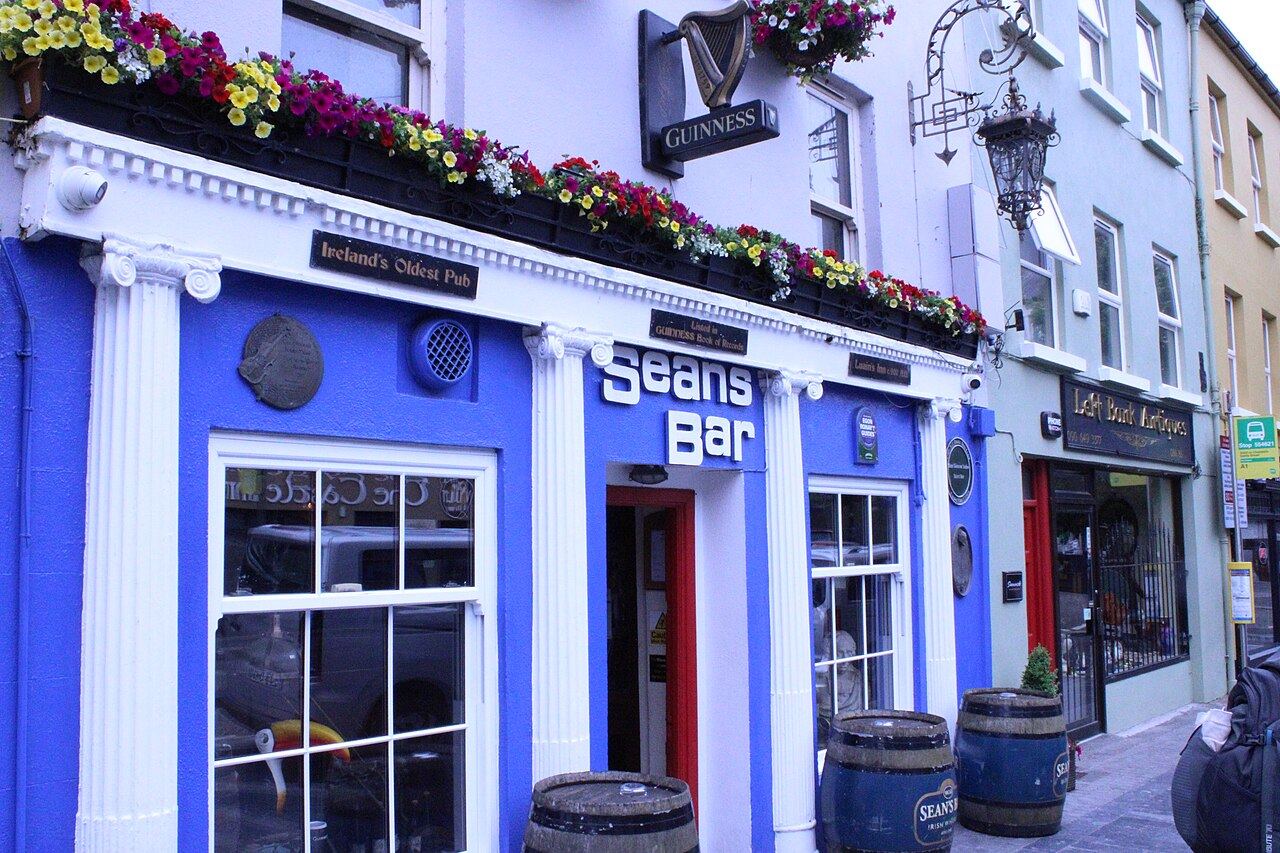 Blue and white front of Sean's Bar with flower boxes and whiskey barrels outside